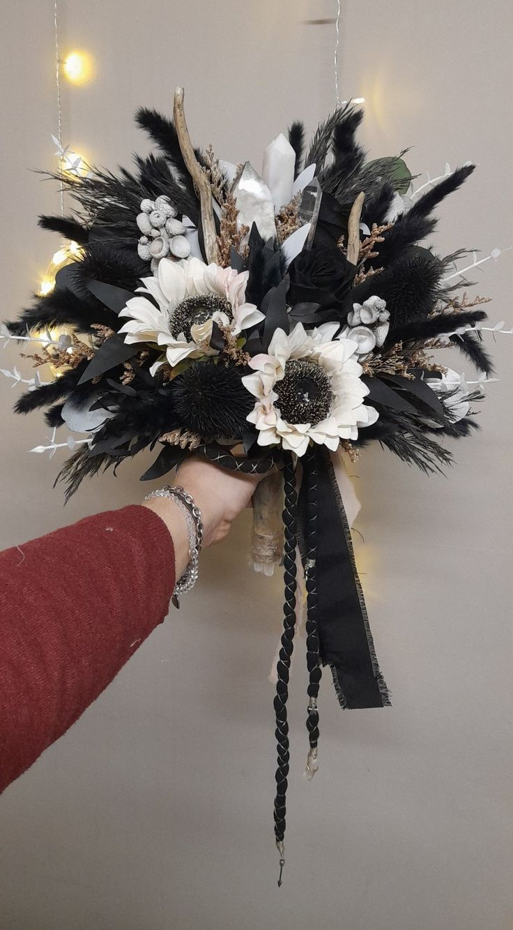 a person is holding a bouquet with feathers and flowers on the wall in front of them