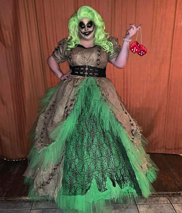 a woman dressed as a skeleton holding a dice and wearing a green dress with feathers