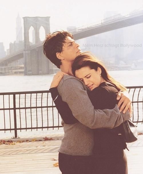 a man and woman hugging in front of the brooklyn bridge