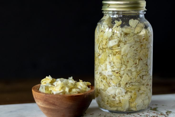 a wooden bowl filled with chopped onions next to a glass jar full of shredded onion