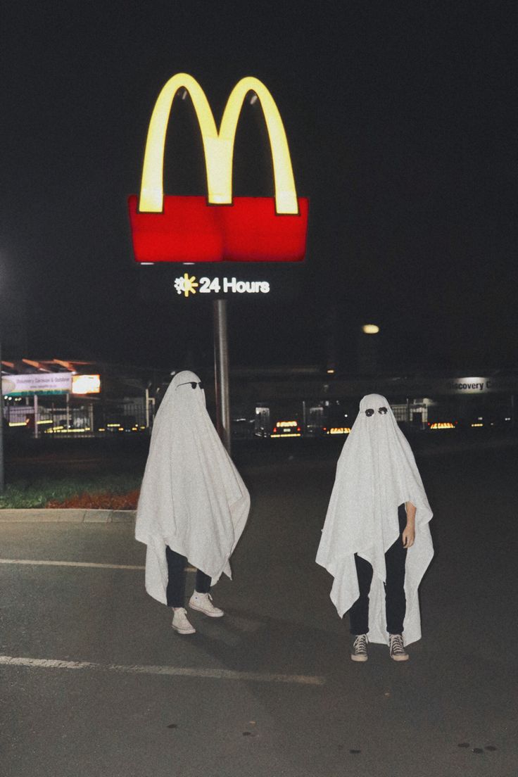 two people dressed in ghost costumes walk past a mcdonald's sign