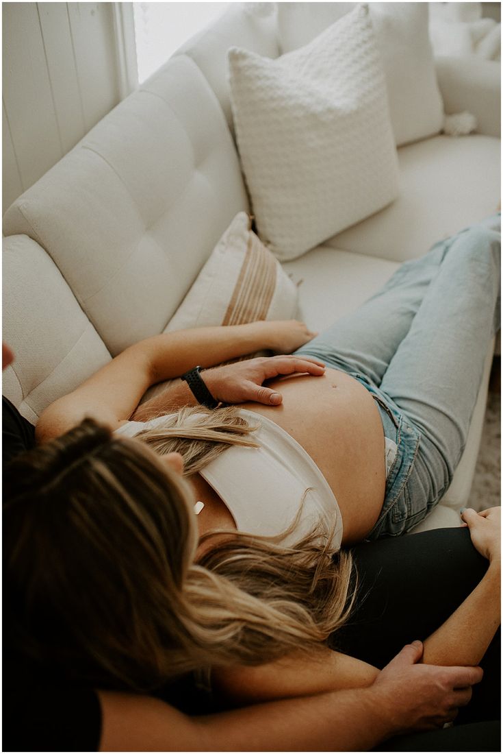 a pregnant woman laying on top of a white couch