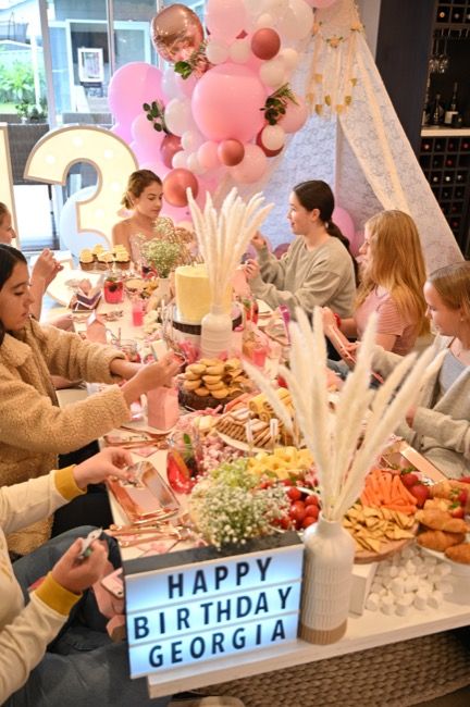 a group of people sitting around a table with food and balloons in the shape of letters