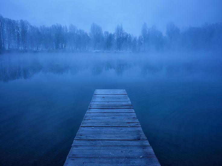 a wooden dock sitting on top of a lake next to a foggy forest filled sky