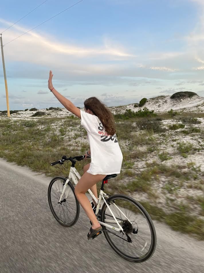 a woman riding a bike down a road with her arms in the air and one hand up