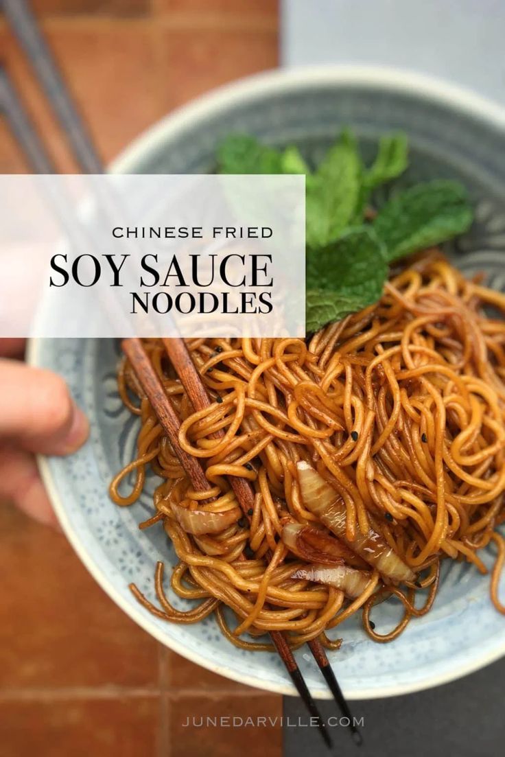 someone holding a bowl of noodles with chopsticks in it and the words soy sauce noodles