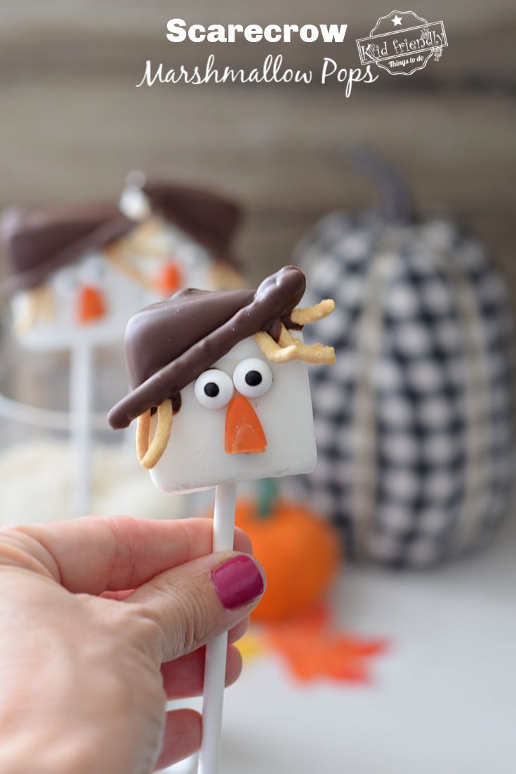 a hand holding a marshmallow pops decorated like a scarecrow