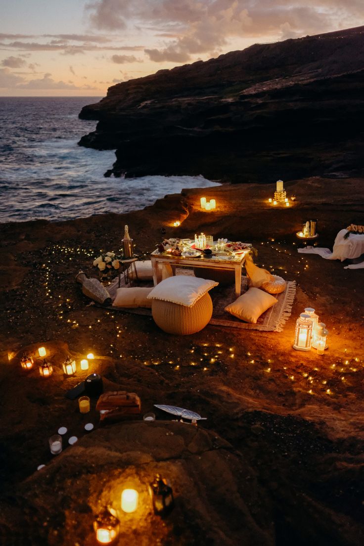 an outdoor seating area is lit up at night by candles on the rocks near the ocean