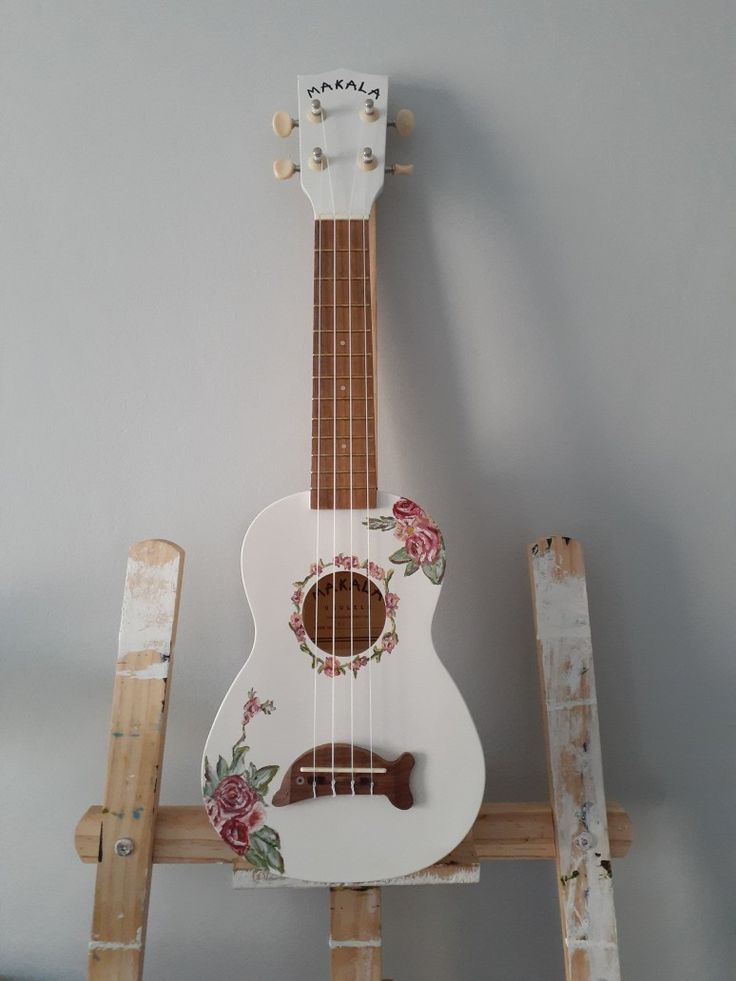 a white ukulele sitting on top of a wooden stand with flowers painted on it