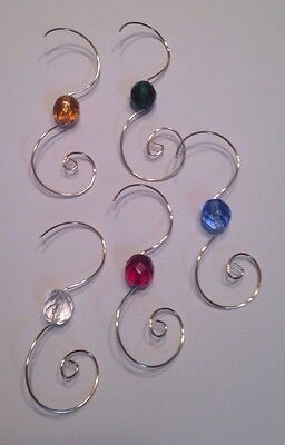 four different colored glass beads are hanging from silver earwires on a white surface