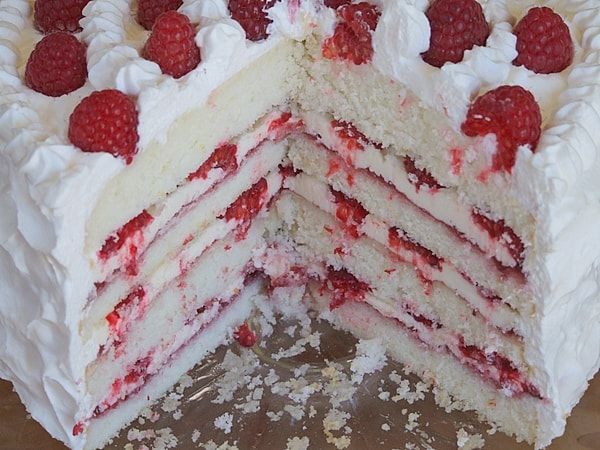 a cake with white frosting and raspberries is cut in half to show the layers