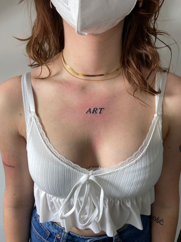 a woman wearing a face mask with the word art tattooed on her chest