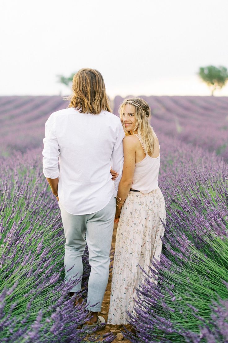 a man and woman walking through a lavender field