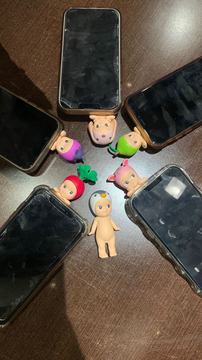 five cell phones sitting on top of a table next to each other with small figures in front of them