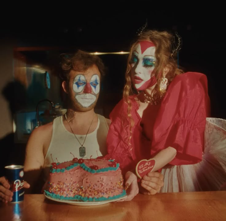 two people with face paint on their faces sitting at a table in front of a cake