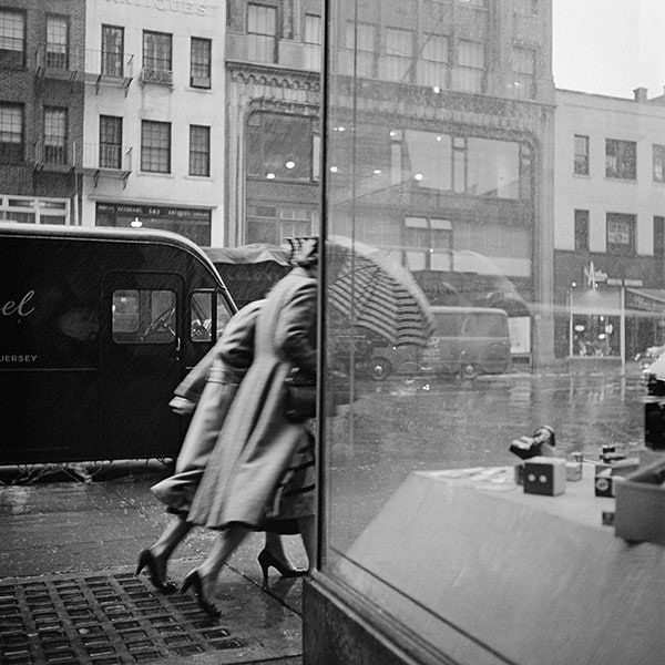 a woman walking past a store window with an umbrella in it's raincoat