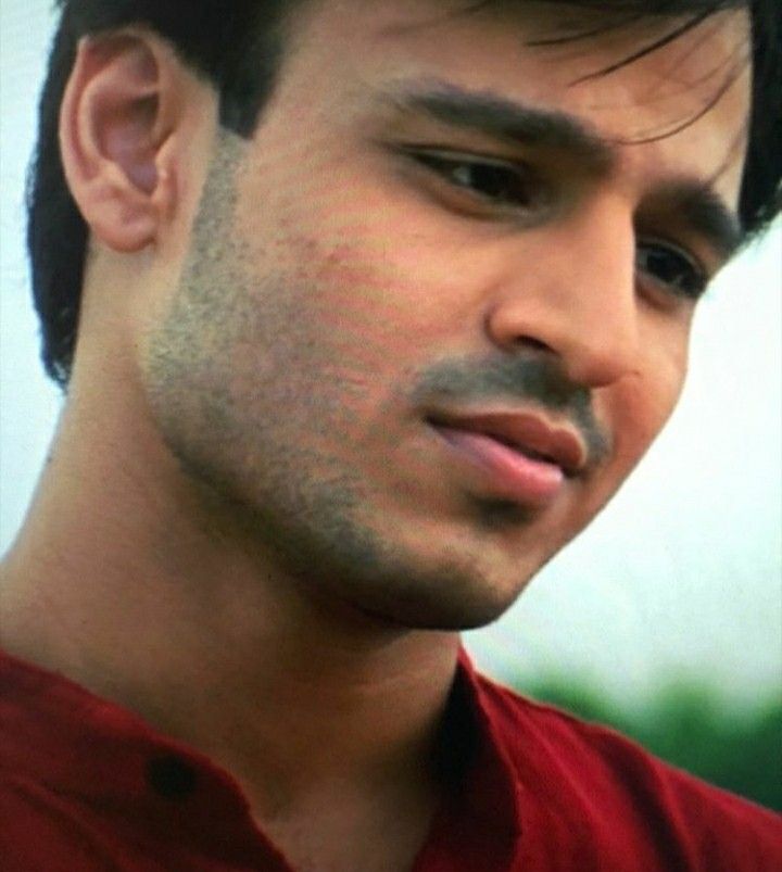 a close up of a young man wearing a red shirt and looking at the camera