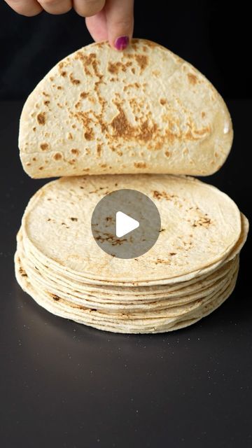 a stack of tortilla sitting on top of a black counter next to a person's hand