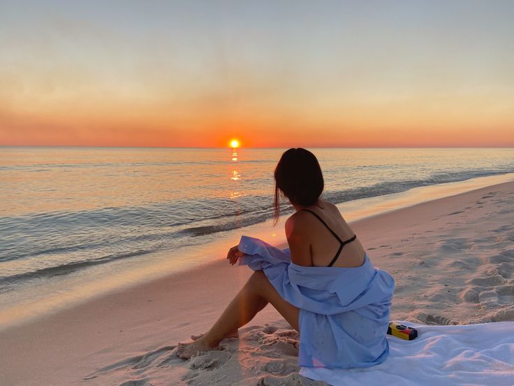 a woman sitting on the beach watching the sunset