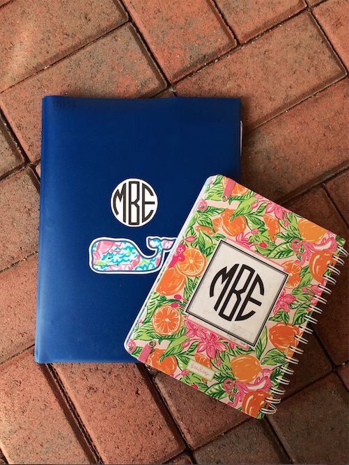 two notebooks with monogrammed stickers on them sitting next to each other