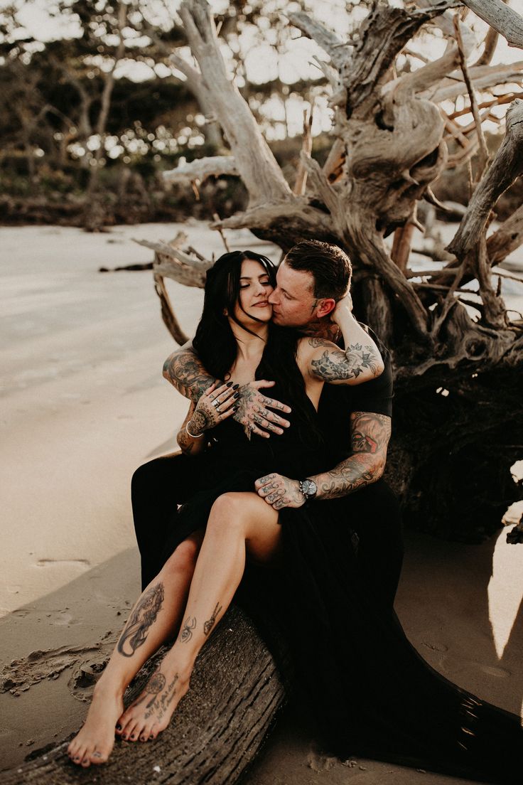 a man and woman sitting on top of a tree trunk kissing in front of the ocean