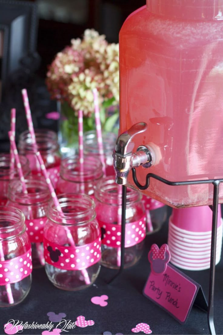 there are many pink cups with minnie mouse straws in them and one has a drink dispenser on it