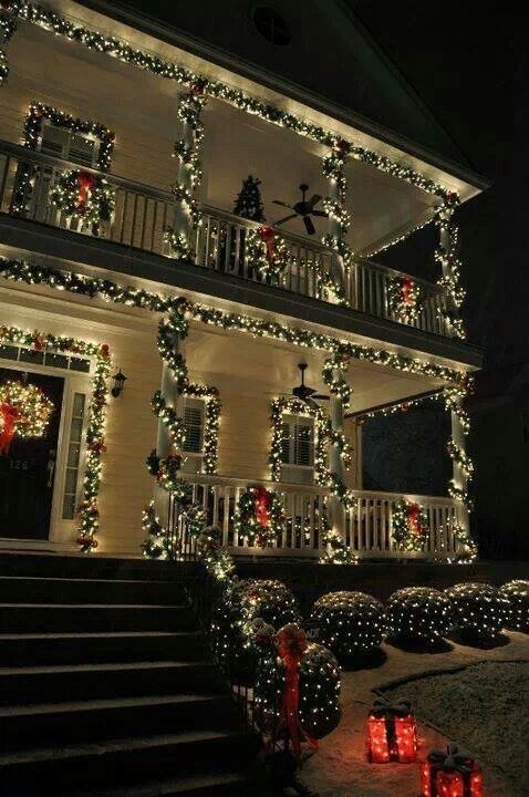 christmas lights decorate the outside of a house in front of stairs and trees with wreaths on them