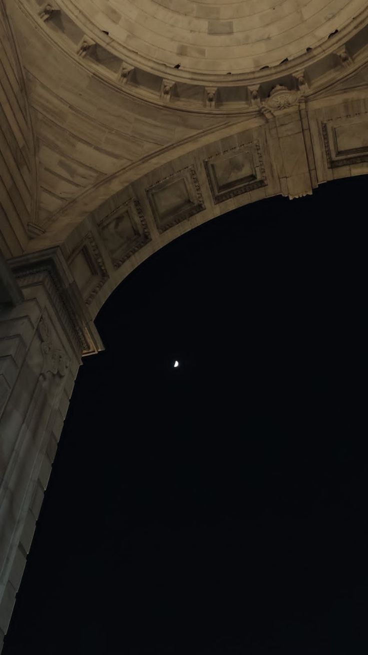 an arch with a clock on the top and moon in the sky above it at night