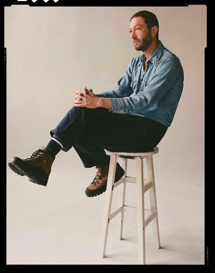 a man sitting on top of a stool with his feet up in the air and looking off to the side