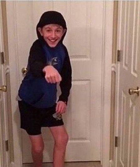 a young boy is standing in front of the door with his hand out and smiling