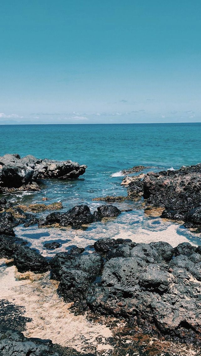 an ocean view with rocks and water in the foreground, blue sky above it