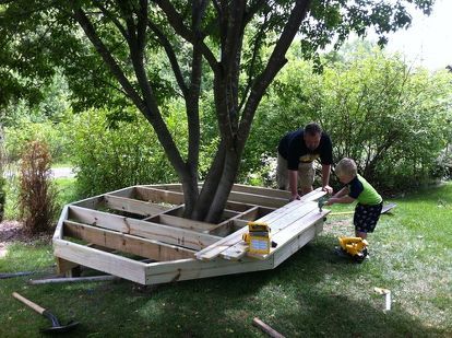 two men working on a wooden boat in the grass next to a tree and tools