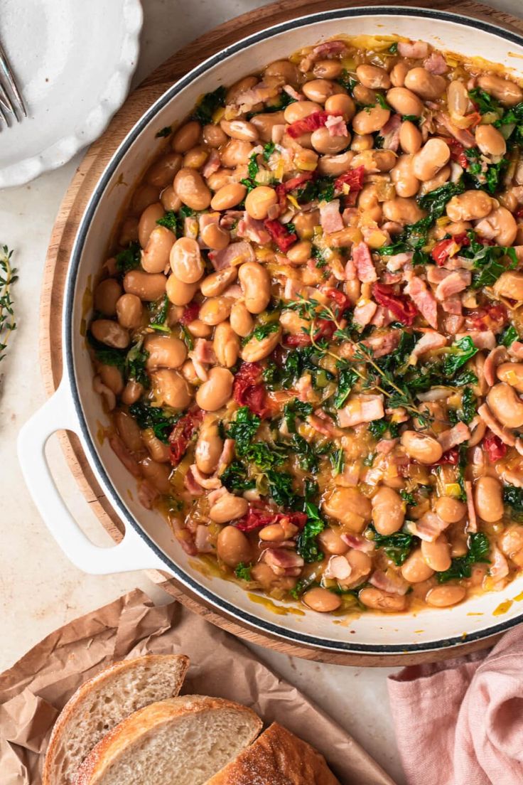 a pot filled with beans and spinach on top of a table next to bread