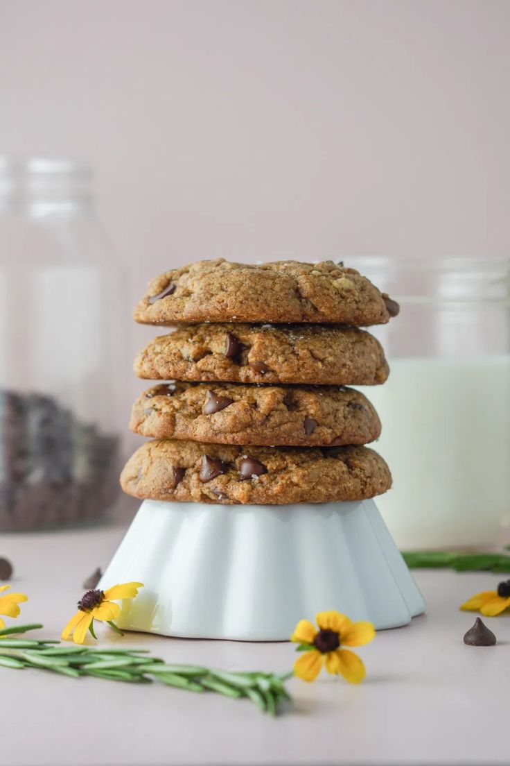 chocolate chip cookies stacked on top of each other next to a glass of milk and flowers