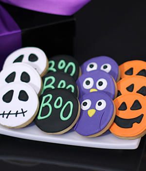 decorated cookies in the shape of owls and pumpkins are on a plate next to a purple ribbon