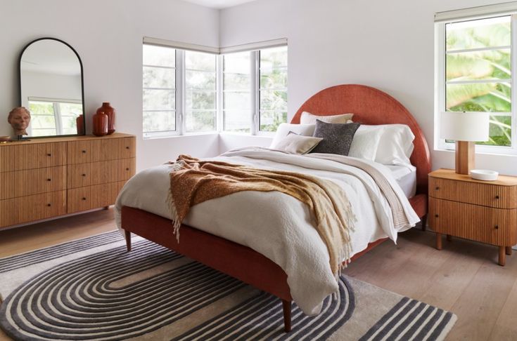 a bedroom with a bed, dressers and mirror on the wall in front of two windows