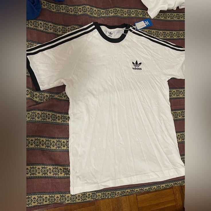 Brand New Never Worn, It Has A Small Stain On The Back ( 3rd Picture) Length~ 25 In Pit To Pit~ 18 In Classic Crew Neck Top With Three Stripes, Basic Adidas Tops With Three Stripes, Adidas White Fitted T-shirt, Classic Adidas Short Sleeve Tops, Classic Adidas Cotton Tops, Adidas Sporty Cotton Shirt, Sporty Adidas Cotton Shirt, White Short Sleeve Tops With Three Stripes, Classic White Top With Three Stripes