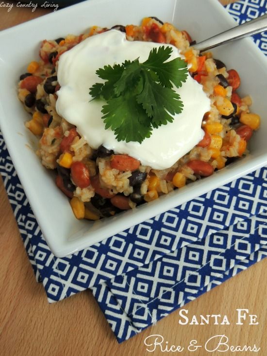 a square white bowl filled with rice and beans topped with sour cream on the top