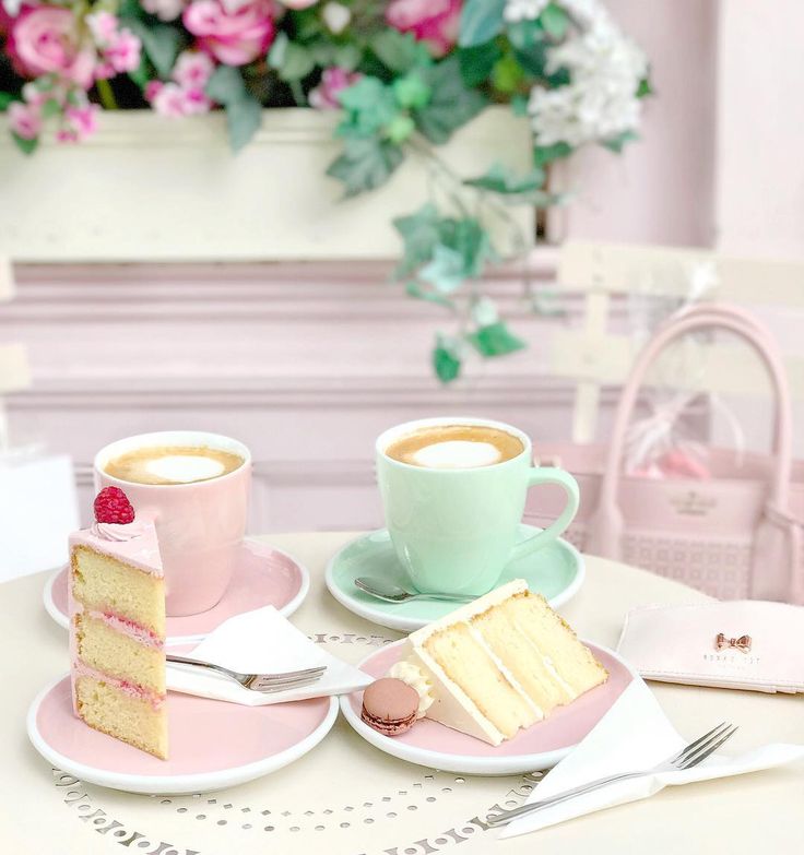 two slices of cake on pink plates with cups of coffee and flowers in the background