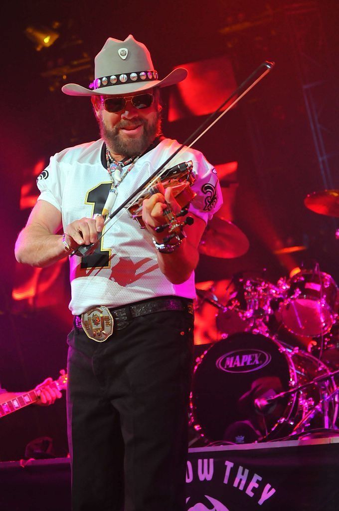 a man wearing a cowboy hat and holding a violin in his right hand while standing on stage