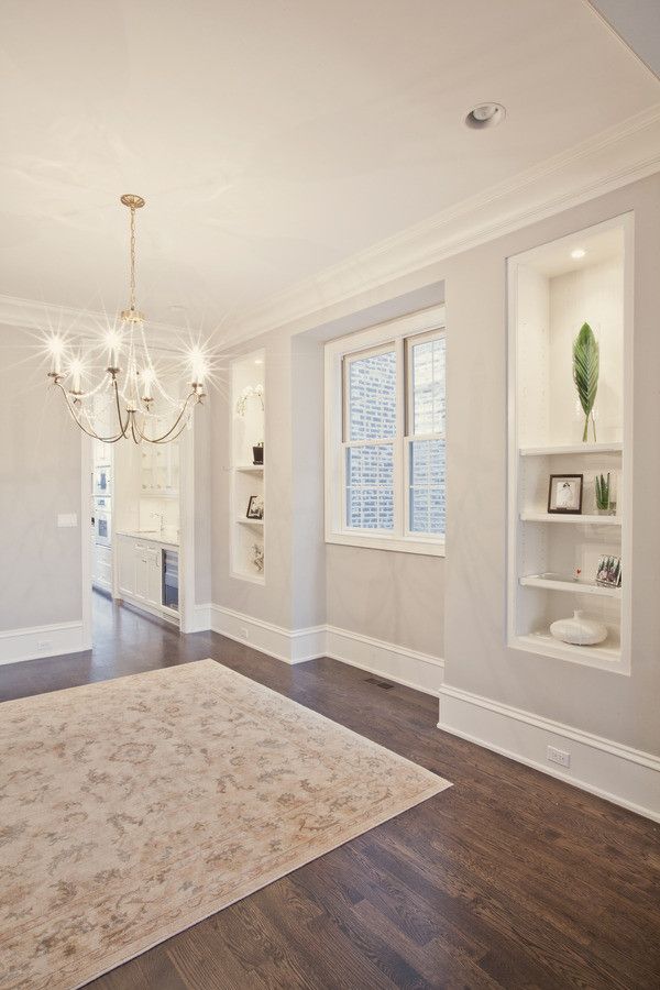 an empty living room with white walls and wood flooring, chandelier hanging from the ceiling