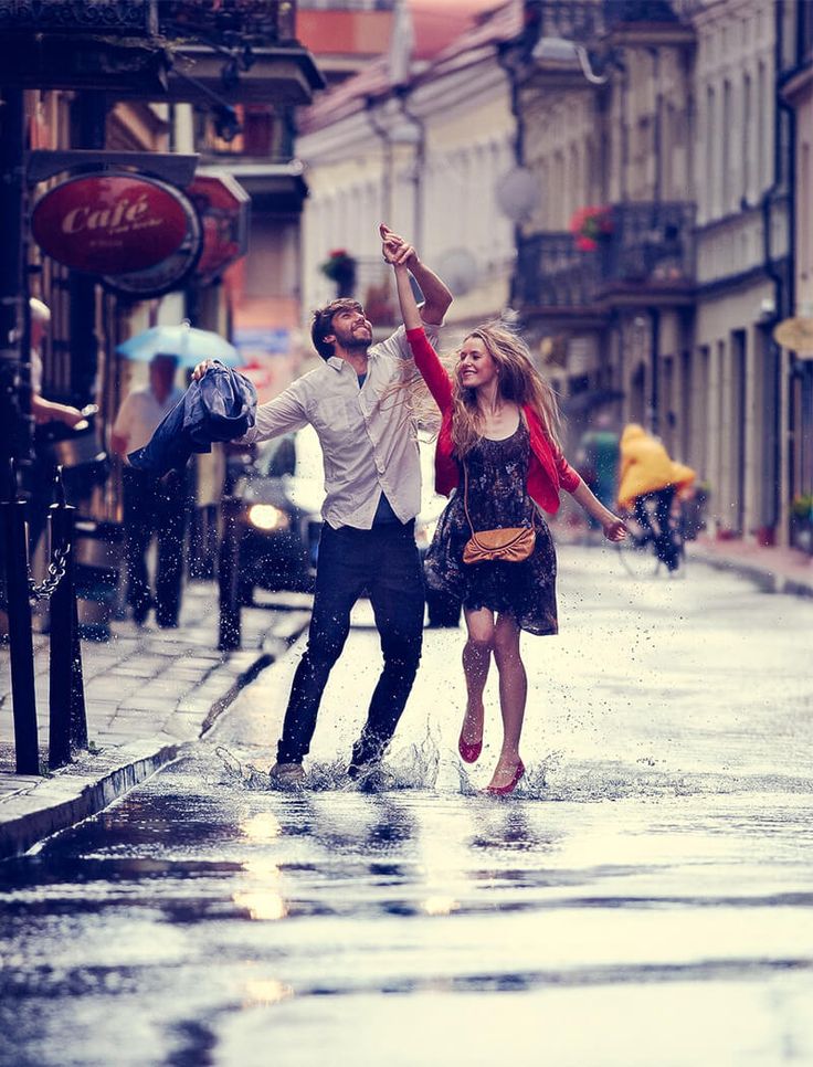 a man and woman are dancing in the rain on a city street with umbrellas