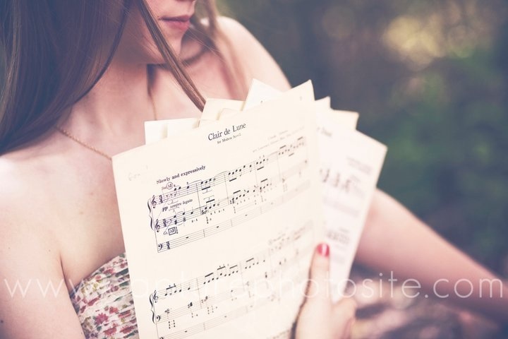 a woman is holding sheet music in her hands and looking at the notes she has placed on her chest