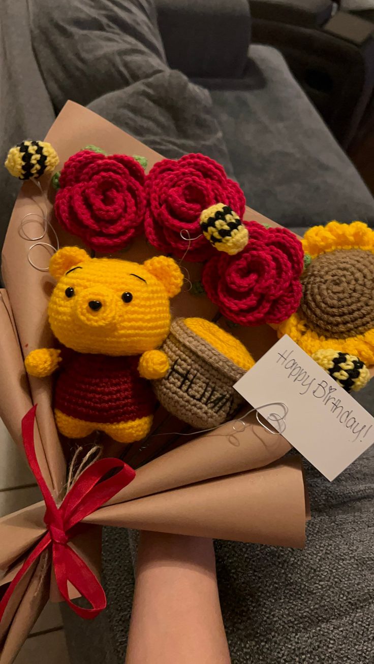 a person holding a bunch of knitted teddy bears and flowers in their lap with a sign on it