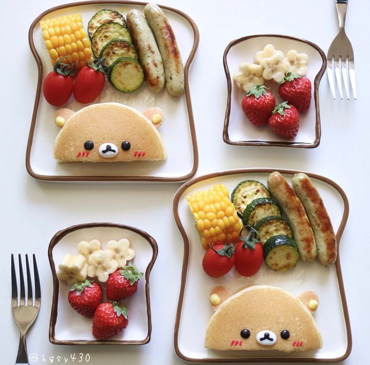 four plates with food shaped like animals and vegetables on them, including strawberries, bananas, cucumbers, and other foods