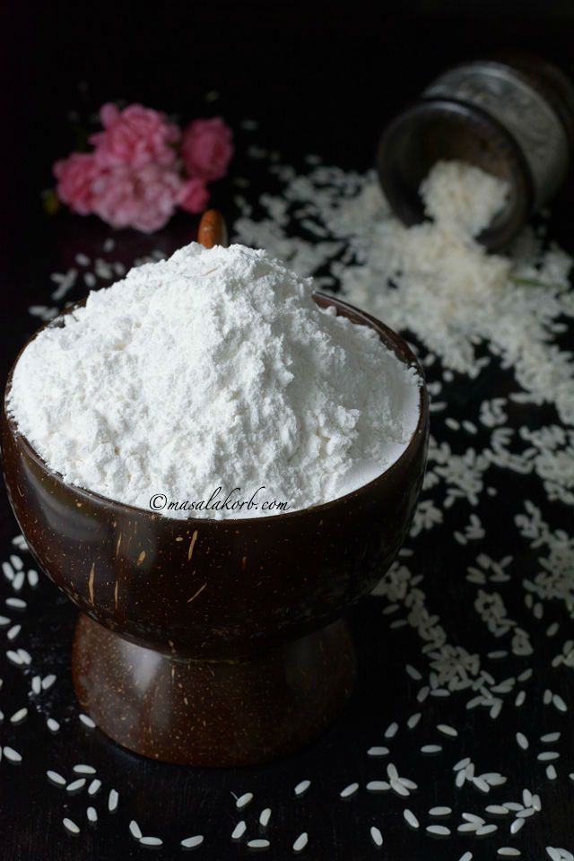 a wooden bowl filled with white powder on top of a black table next to flowers