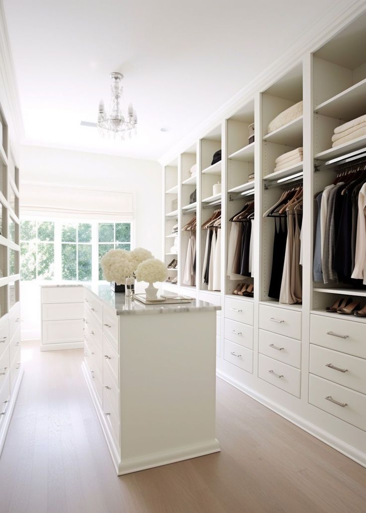 a walk in closet filled with lots of white drawers and shelves next to a chandelier