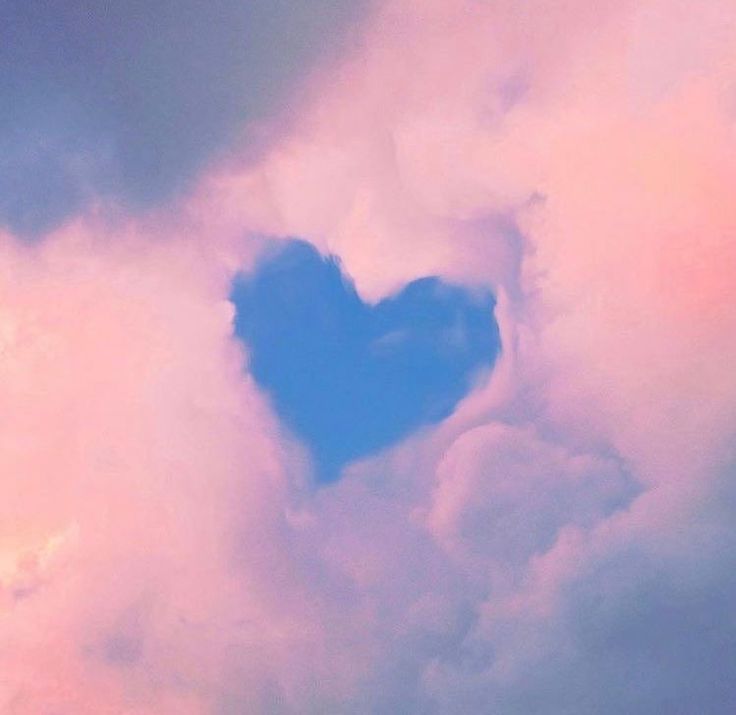 a heart shaped cloud in the sky with pink and blue clouds behind it on a sunny day