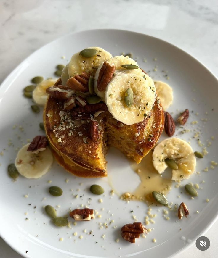 a white plate topped with pancakes covered in bananas and nuts