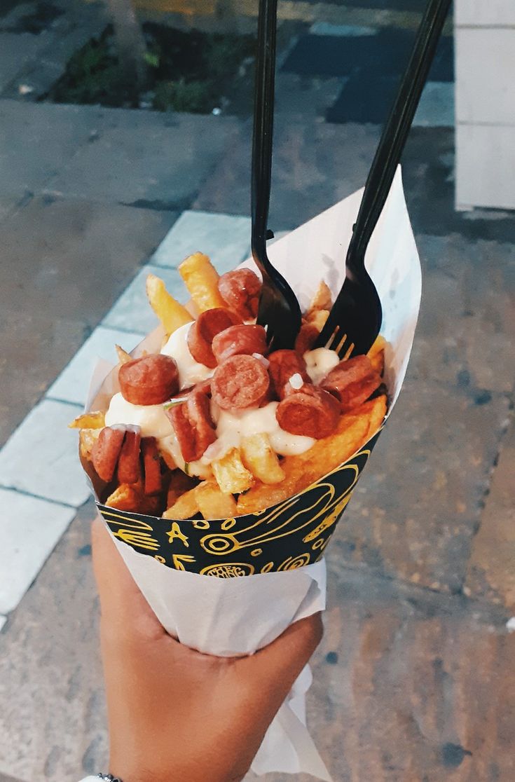 a person holding up a paper basket filled with french fries and other food on top of it